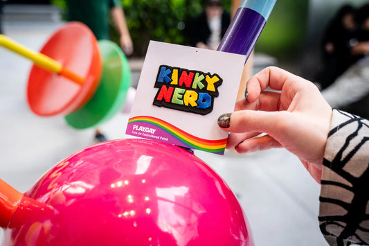 Kinky Nerd rainbow patch on PlayGay card, held by hand with rainbow nails.