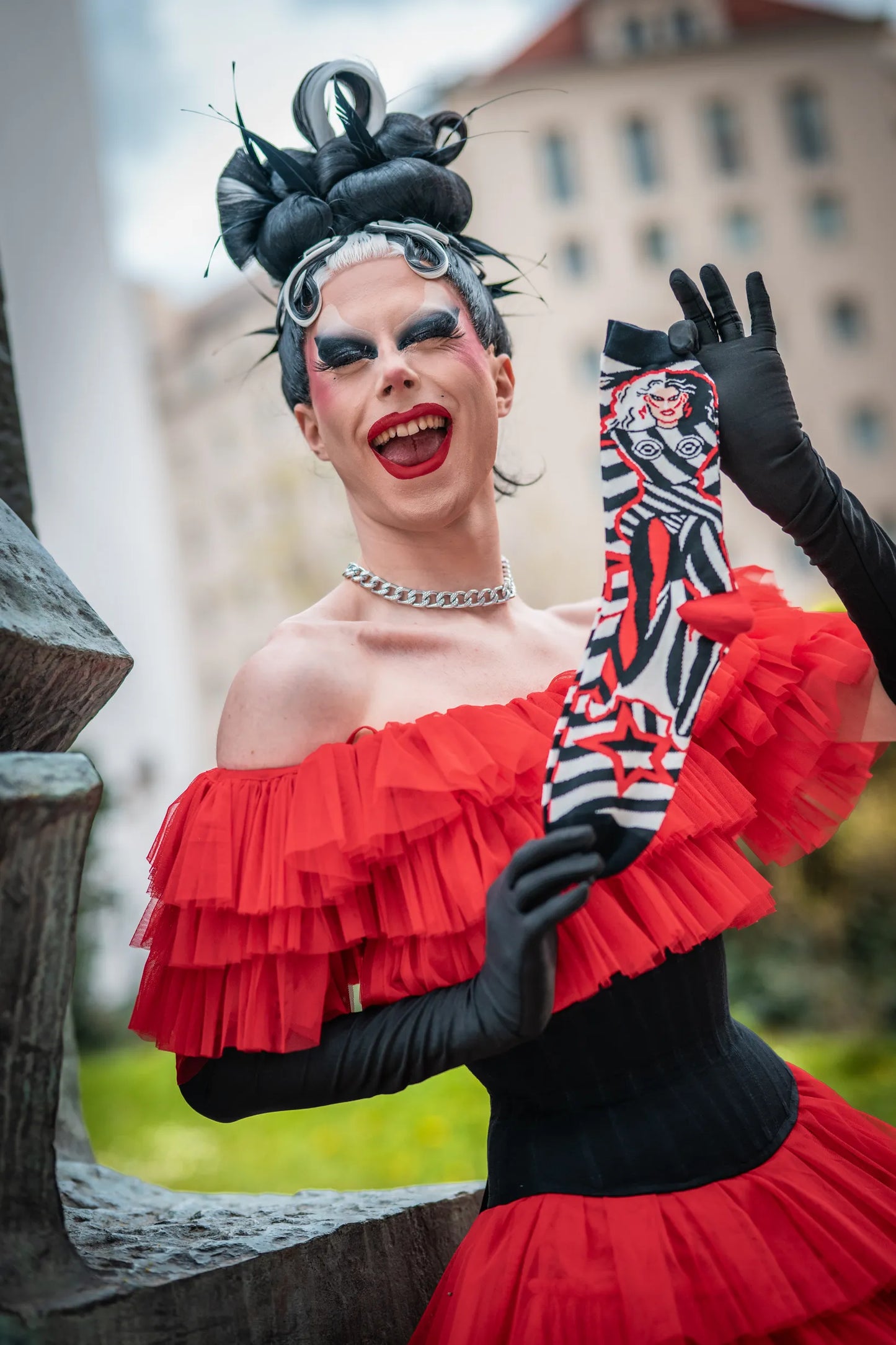 Metamorkid, the finalist from drag race Germany, is posing with her official play.gay socks collaboration in a red dress and black gloves.
