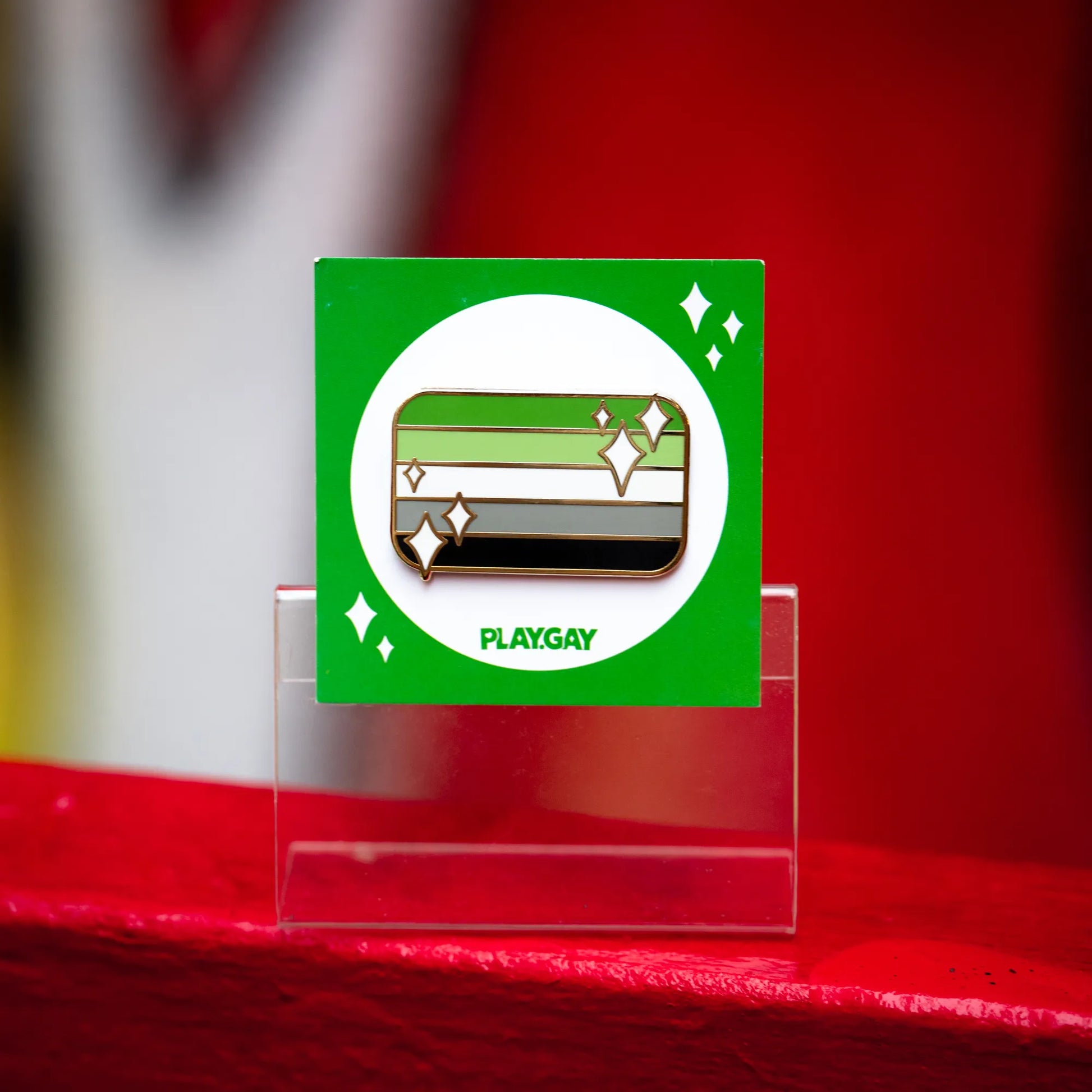 Aromantic pride flag enamel pin with green, light green, white, grey, and black stripes with white sparkle accents on a green PlayGay card.