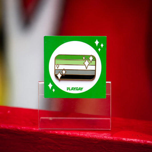 Aromantic pride flag enamel pin with green, light green, white, grey, and black stripes with white sparkle accents on a green PlayGay card.