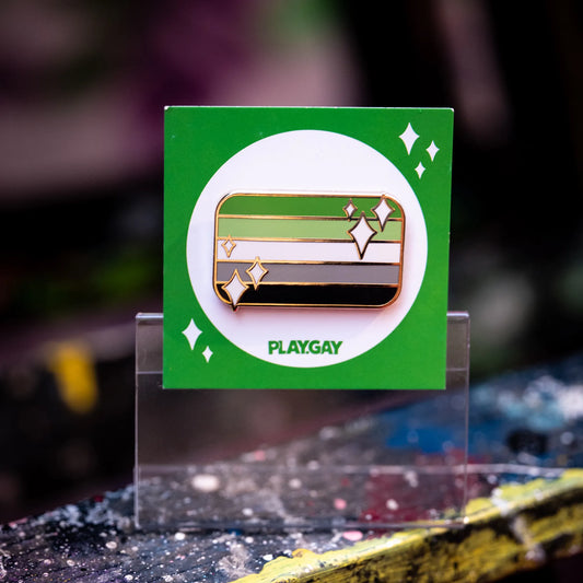 Aromantic pride flag enamel pin with green, light green, white, grey, and black stripes with white sparkle accents on a green PlayGay card. 