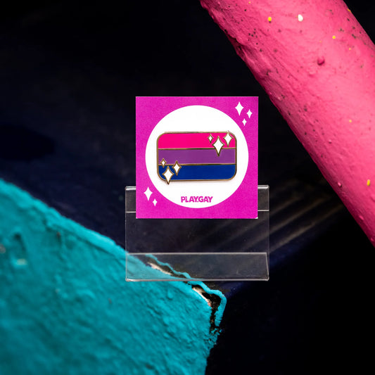 Bisexual pride flag enamel pin in pink, purple, and blue stripes with white sparkle accents, mounted on a magenta PlayGay backing card.
