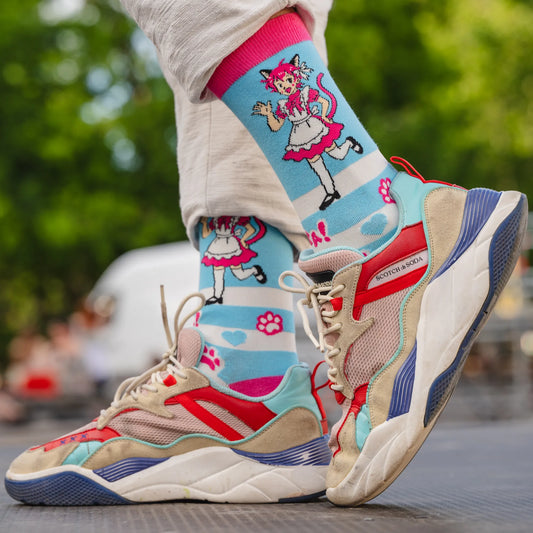 Close-up of person wearing blue catboy socks with pink-haired maid character and paw prints, paired with colorful sneakers outdoors.