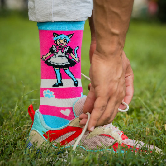Close-up of person wearing pink socks with anime-style blue-haired catboy in a maid outfit, tying colorful sneakers on grass.