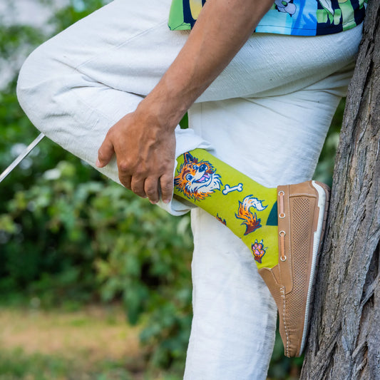 Person wearing green socks with a cartoon wolf, bones, and paw prints, posing outdoors with one foot against a tree.