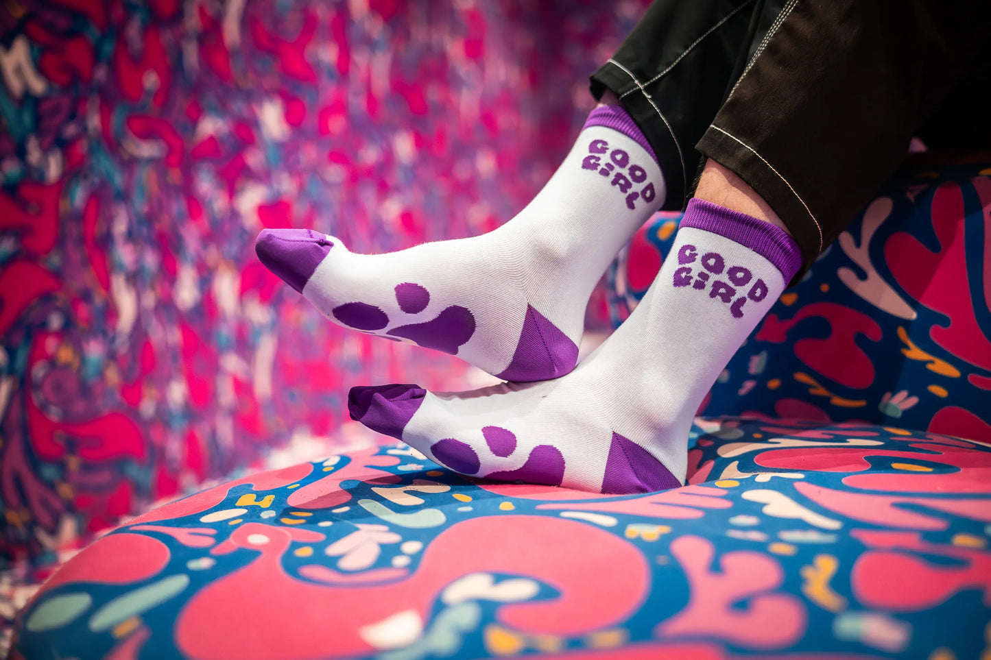 Person wearing 'Good Girl' socks on a colorful patterned couch