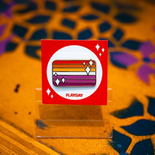 Lesbian pride flag enamel pin with orange, white, and pink stripes, highlighted with white sparkle accents on an orange PlayGay backing card.