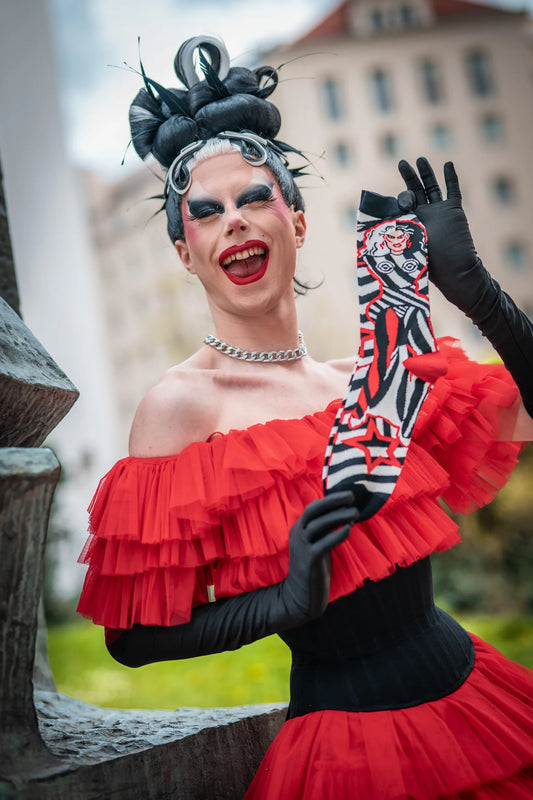 Metamorkid, the finalist from drag race Germany, is posing with her official play.gay socks collaboration in a red dress and black gloves. 