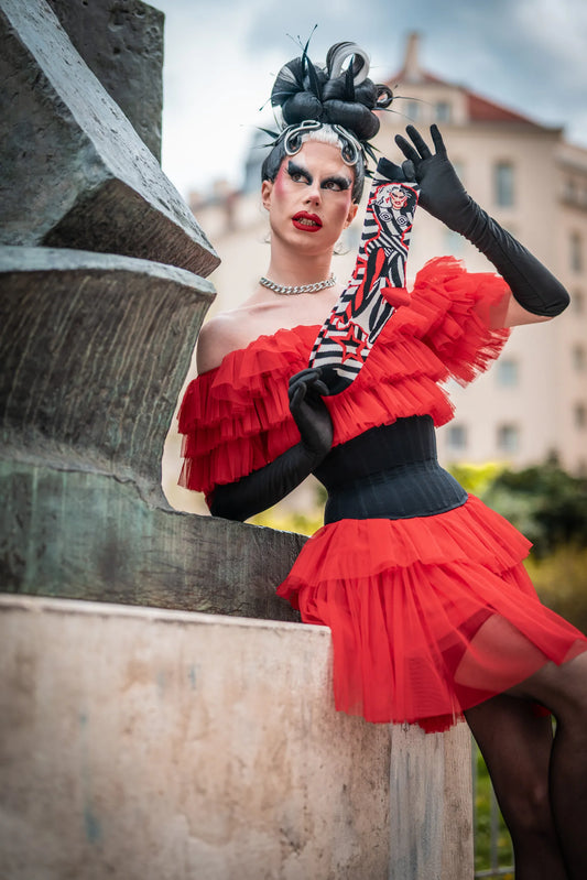 Metamorkid, the finalist from drag race Germany, is posing with her official play.gay socks collaboration in a red dress and black gloves. 