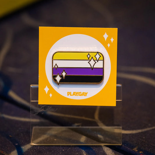 Nonbinary pride flag enamel pin featuring yellow, white, purple, and black horizontal stripes with sparkles, on a yellow PlayGay card.