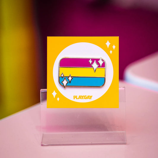 Pansexual pride flag enamel pin with yellow, pink, and blue horizontal stripes with white sparkle accents, mounted on a PlayGay backing card.