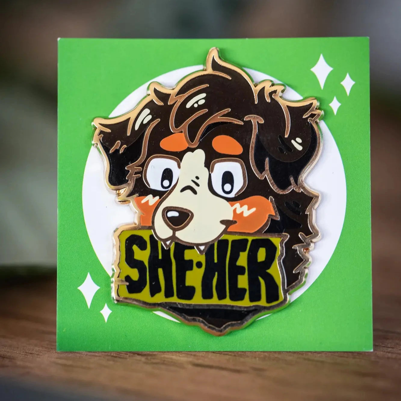 PlayGay Pronoun Dogs SHE·HER Enamel Pin - dark fluffy dog with SHE·HER banner enamel pin on green backing card