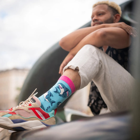 Person sitting casually in sneakers and socks featuring sharks in trans pride colors.